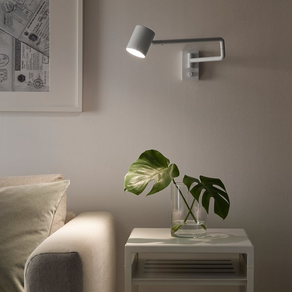 NYMÅNE wall lamp beside bed, lighting bedside table with plant.