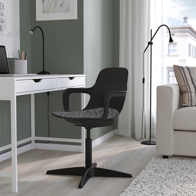 Home office setup with green desk, black chair, and floor lamp. White couch with striped pillows, large window, and cosy rug.