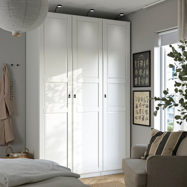 Modern room with tall white PAX wardrobe, striped sofa, and natural light.