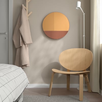 Modern bedroom with large rose-gold SKOGSGRÄNSEN mirror, above wooden chair, reflecting stylish, natural horizon design.