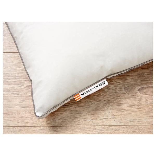 White pillow on wooden floor, showing high-quality cotton and synthetic filling, brand labelled SKOGSOLVON IKEA.
