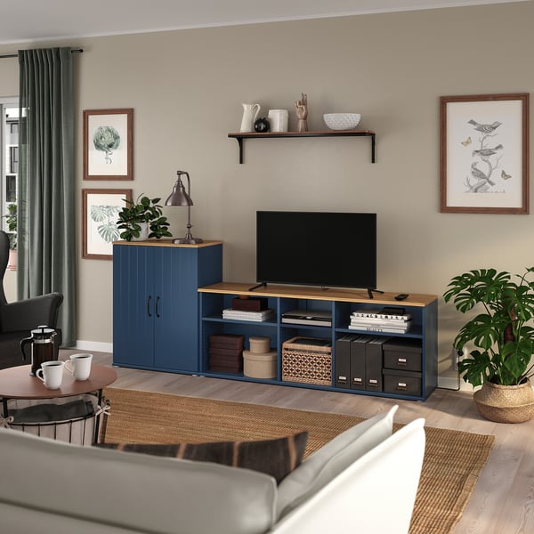 Cosy living room with grey curtains, a grey sofa, a blue tv stand with open and closed storage, a flat-screen tv, plants, and framed art.