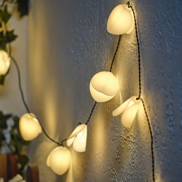 A string of solar-powered, white, teardrop-shaped lights mounted on a blue wall, emitting a warm glow.