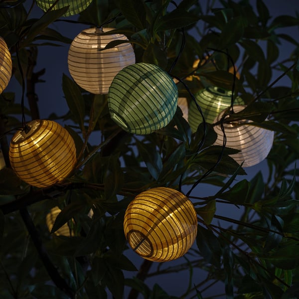 Hanging solar lanterns in green, white, & gold colours, tiny in size, glowing in foliage.