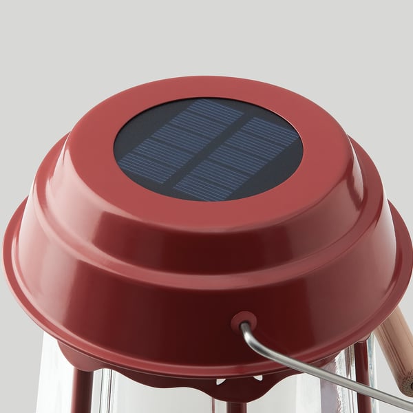 Red solar-powered lamp with smooth, glossy surface, featuring sleek handle and protective glass, sits steadily on three legs.