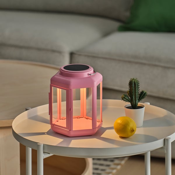 Bright pink solar lantern on a white table, emitting warm light, beside a lemon and a small cactus.