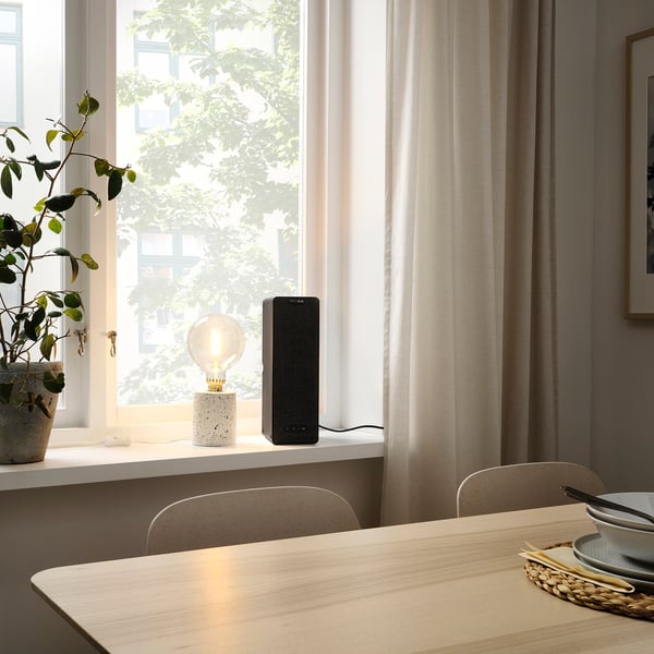 Modern dining area with SYMFONISK wifi speaker on windowsill, lit by sunlight.