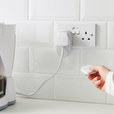 Hand holds remote, controlling plugged-in coffee maker via TRÅDFRI smart outlet.