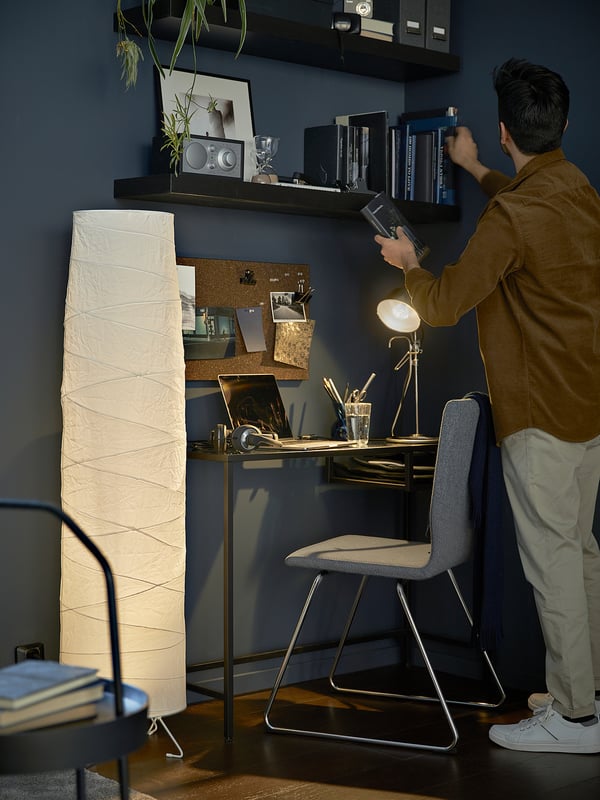 Person at modern glass top desk with lamp, laptop, and bookshelves against blue wall.
