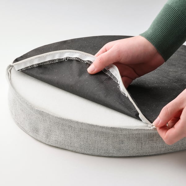 Hand opening grey circular cushion, revealing memory foam and non-slip backing.