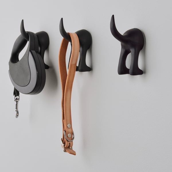 Three black decorative dog head hooks on a wall, one holding a black leash, another a brown leather belt.