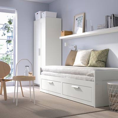 Minimalist white day-bed with drawers, shelf, chair, and table in calm, lit room.