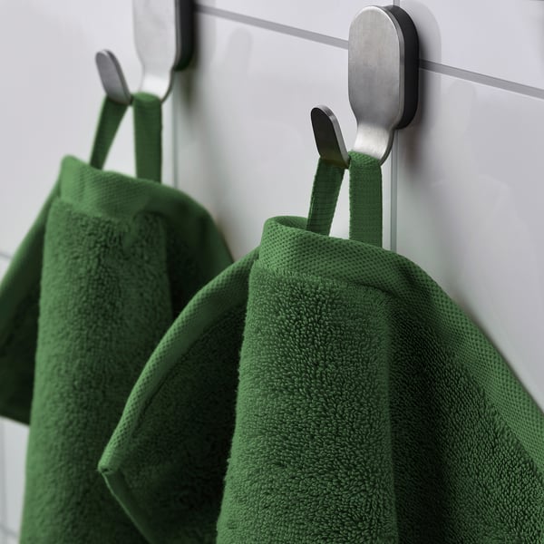 Green towels on modern hooks against a white wall. Textured, absorbent, quality design.
