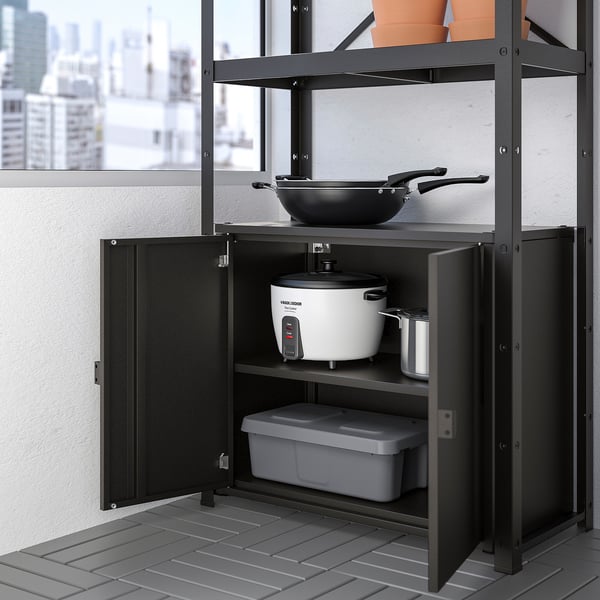 Metal storage shelf with open doors, holding a rice cooker, lidded container, and metal pan, with a city view in the background.