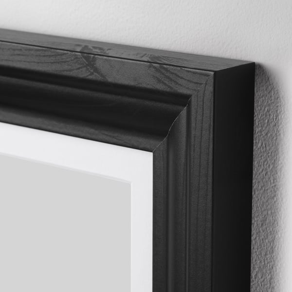 Black picture frame with smooth, sleek edges and a polished look, positioned against a white wall.