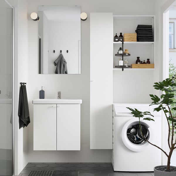 Modern bathroom with ENHET storage, mirror, towels, and stacked clothes. Large washer, plant, black floor tiles.