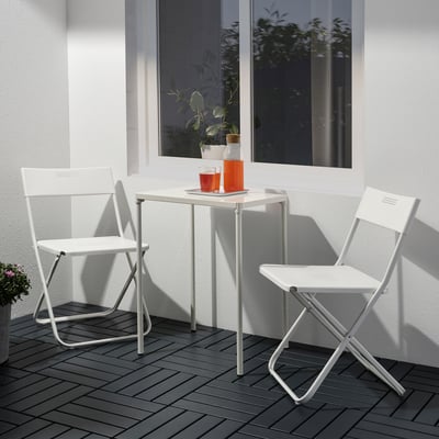 Small outdoor white metal table and chairs set with orange cups, perfect for balconies.