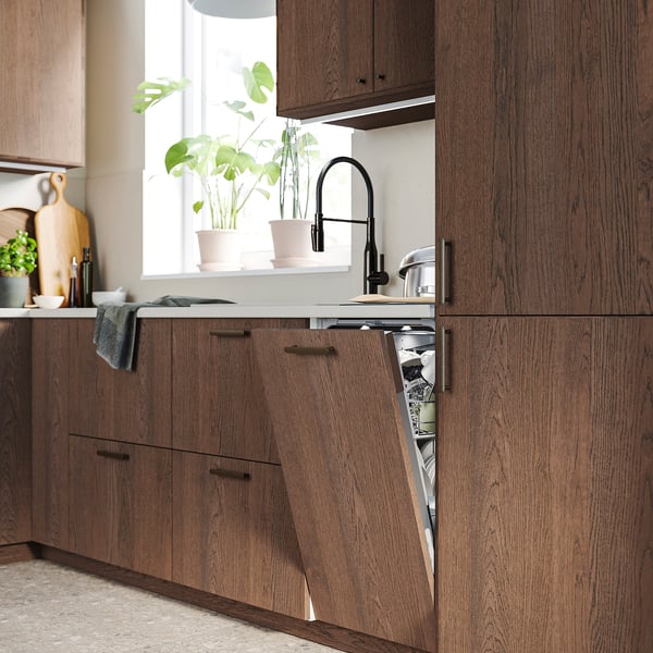 Modern kitchen with dark wood cabinets, an open dishwasher underneath a window with green plants.