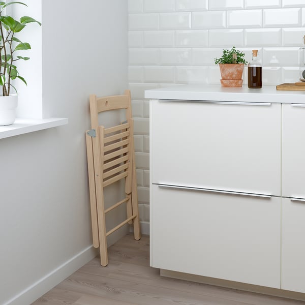 Wooden folding chair leaning against white kitchen cabinet, with a potted plant and oil bottle on the countertop.