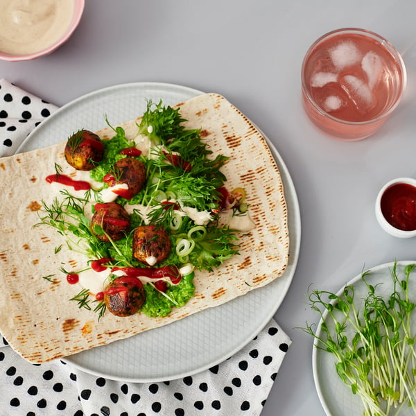 Flatbread wrap with green salad, sauce, and meat on white plate with drink.