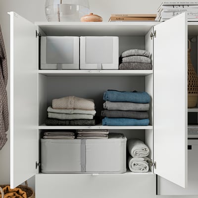 White cabinet with folded clothes, organised in sections, top shelf has a glass vase and stacked books.
