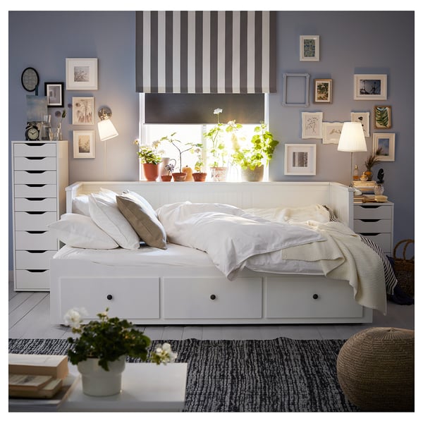 Bright bedroom with white HEMNES daybed, striped curtains, and wall art. Potted plants on window sills, and drawers on either side of bed.