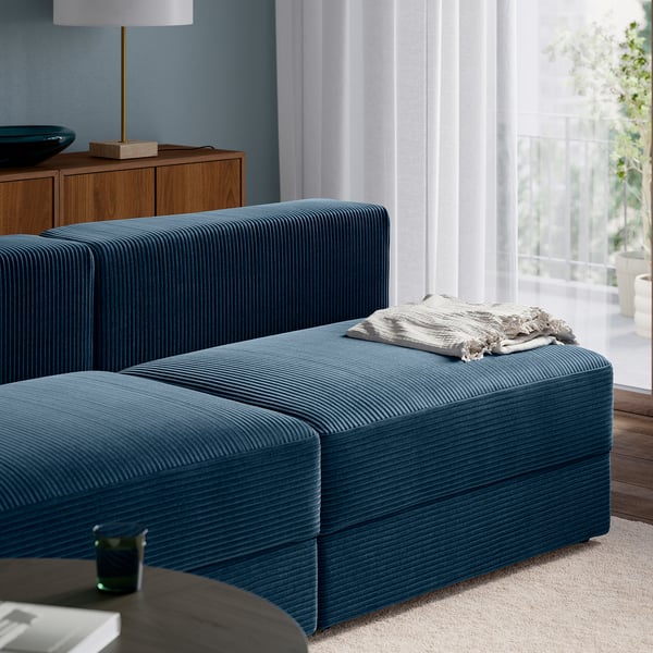 Blue sofa with a blanket, lamp nearby, large windows, wooden floor.