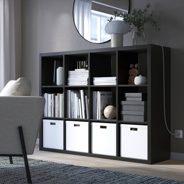 Modern living room with KALLAX bookshelf, books, decor & boxes. Cozy reading nook by armchair, mirror & lamp.