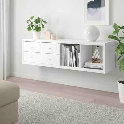 White ikea KALLAX shelves hold books, plants, and decor, narrow with drawers, between wall decor and a sofa.