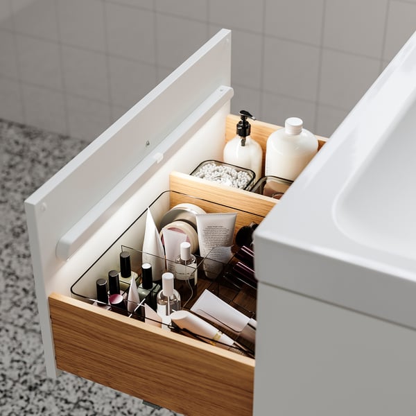 Open wooden drawer with organised toiletries, including nail polishes and bottles. Soft light automatically illuminates the contents.