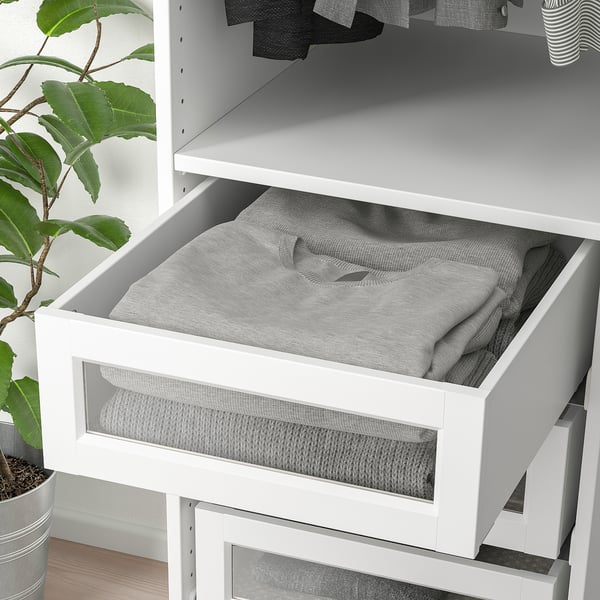A white wardrobe drawer with glass front, holding folded grey clothes, part of a pax system.