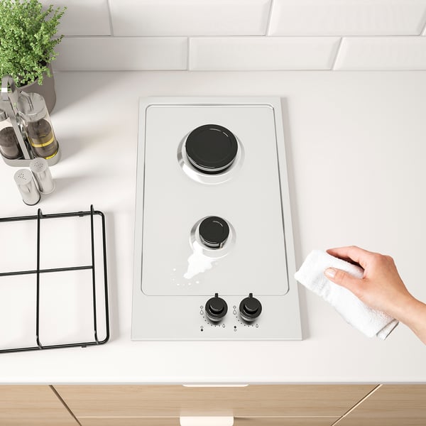 A modern kitchen scene featuring a two-burner gas stove with digital controls being cleaned with a cloth.