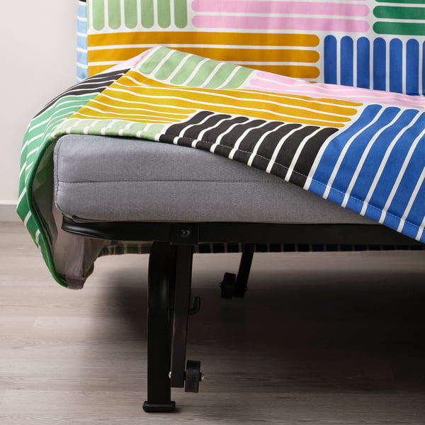 Bed with colourful, striped quilt and grey mattress on black metal base with wheels.