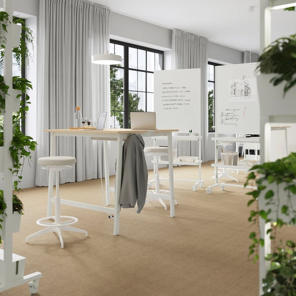 Modern office with MITTZON tables, stools, large windows, whiteboards, and plants for a bright, productive space.