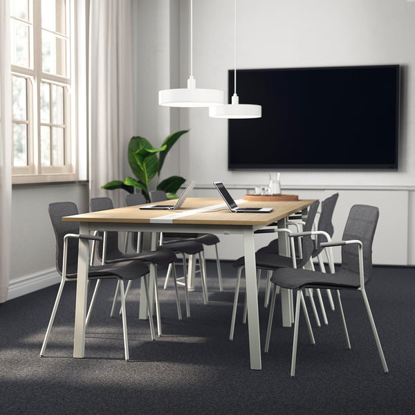MITTZON conference table: modern, rectangular, wooden top with metal base, surrounded by black fabric chairs, and a large tv. Ideal for meetings.