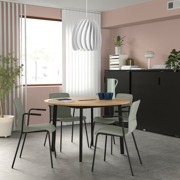 Oak conference table with green chairs by large window, black cabinet, plants.