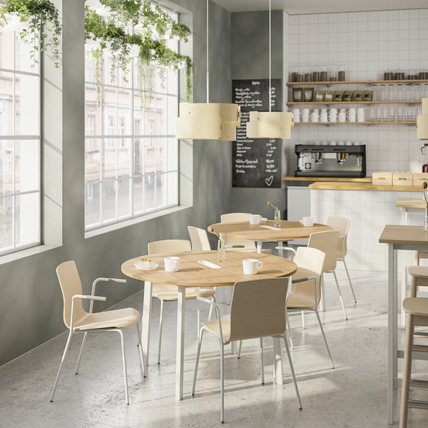 Minimalist café with wooden tables, light chairs, plants, and coffee machines.