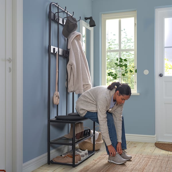 Person tying shoes near hall stand with hooks, shelves, and bench for storage.