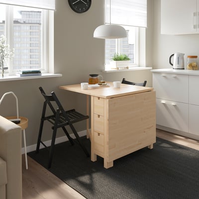 Nordic-style gateleg table in kitchen with drawers, natural finish, black chairs, white cabinets, wooden floor.