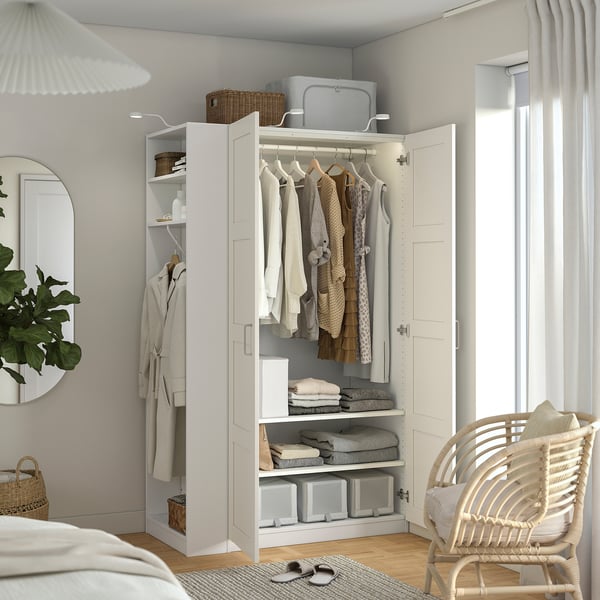 White PAX wardrobe with hanging clothes, folded clothes, and storage boxes.