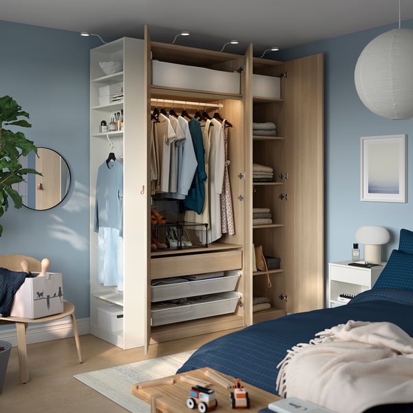 Bedroom with open wooden wardrobe: hanging clothes, drawers, shelves; blue walls, bed, toys.