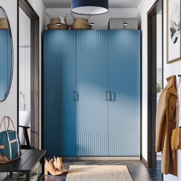 Modern entryway with a tall blue PAX wardrobe, sleek design, surrounded by a round mirror, coat hooks, and a small bench.