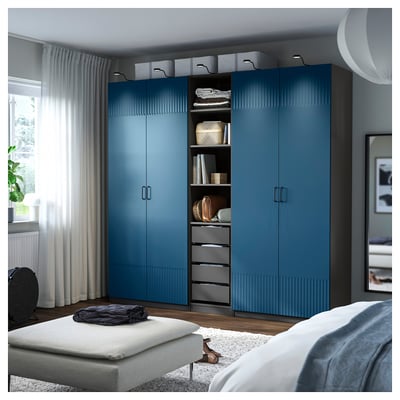 A blue PAX wardrobe with a textured door, standing tall beside a bed. It integrates shelves and drawers, offering ample storage.