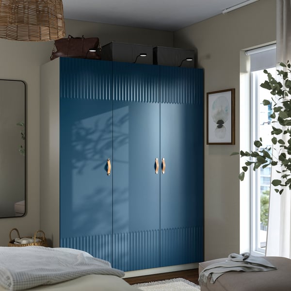 Modern bedroom with a tall blue wardrobe with soft-close doors and storage boxes. Flanked by a mirror and plant.