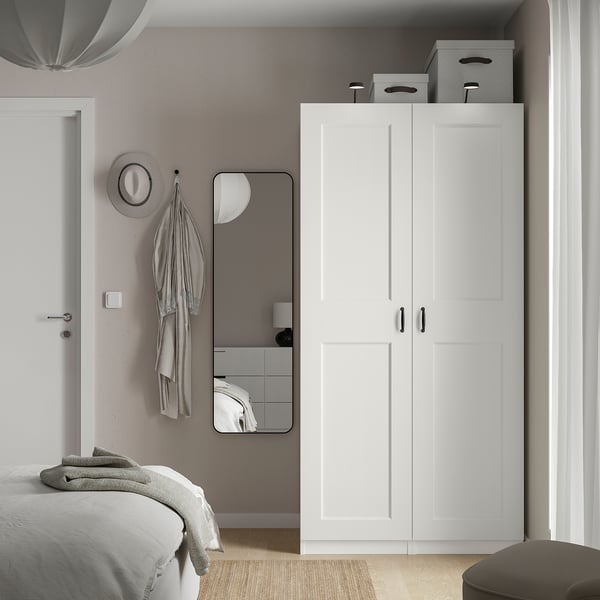 White PAX wardrobe & mirror beside bed, double doors, mesh baskets, modern design.
