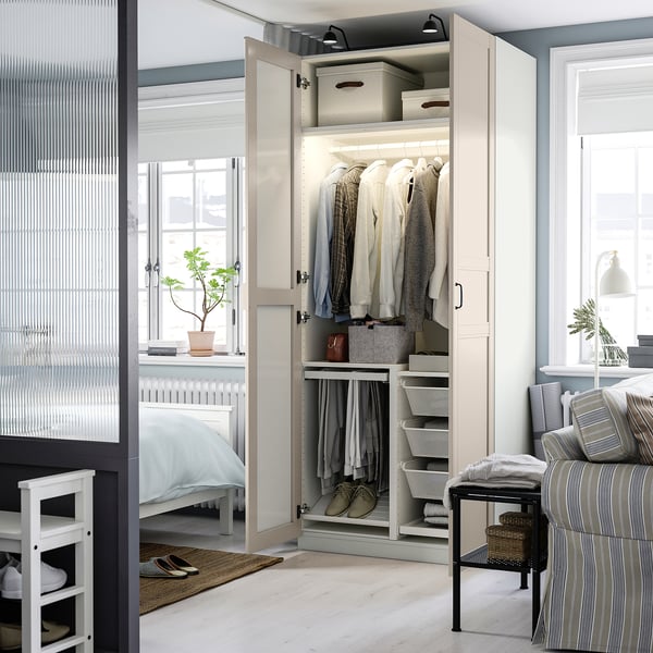 Bedroom with white PAX wardrobe, clothes, cushioned chair, plant, and window.