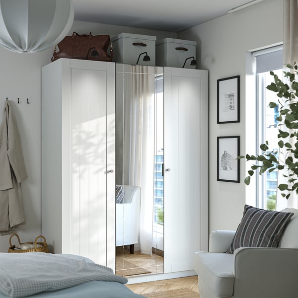 A PAX wardrobe combination in white, with mirrored doors reflecting room decor. Its larger than the nearby bed, offering ample storage.