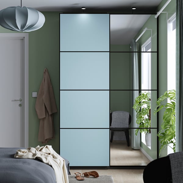 Modern bedroom with blue PAX wardrobe, green walls, plants, and mirrored doors. White bed, robe, grey chair, and large plant.