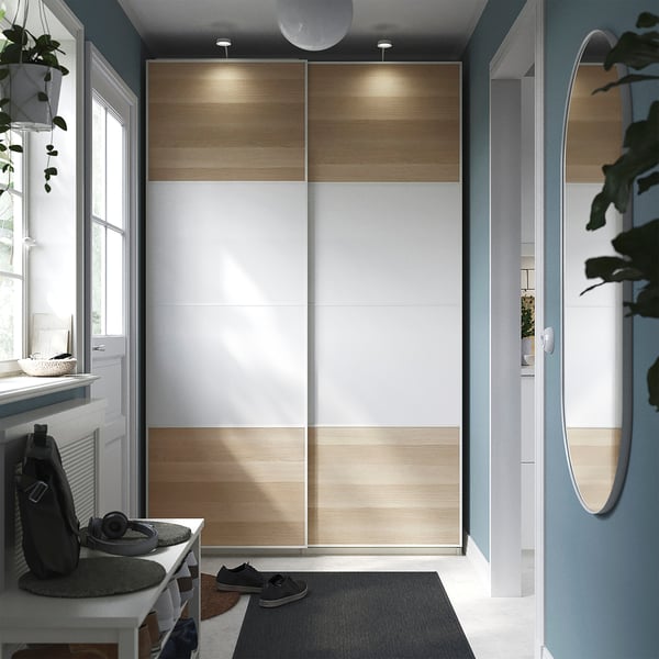 Modern entryway with a PAX wardrobe featuring sliding wooden doors, a white console table with a black bag, and potted plants.