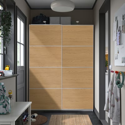 Large wooden PAX wardrobe with sliding doors in entrance hall, taller than nearby table, with shoes, bags, and hooks.